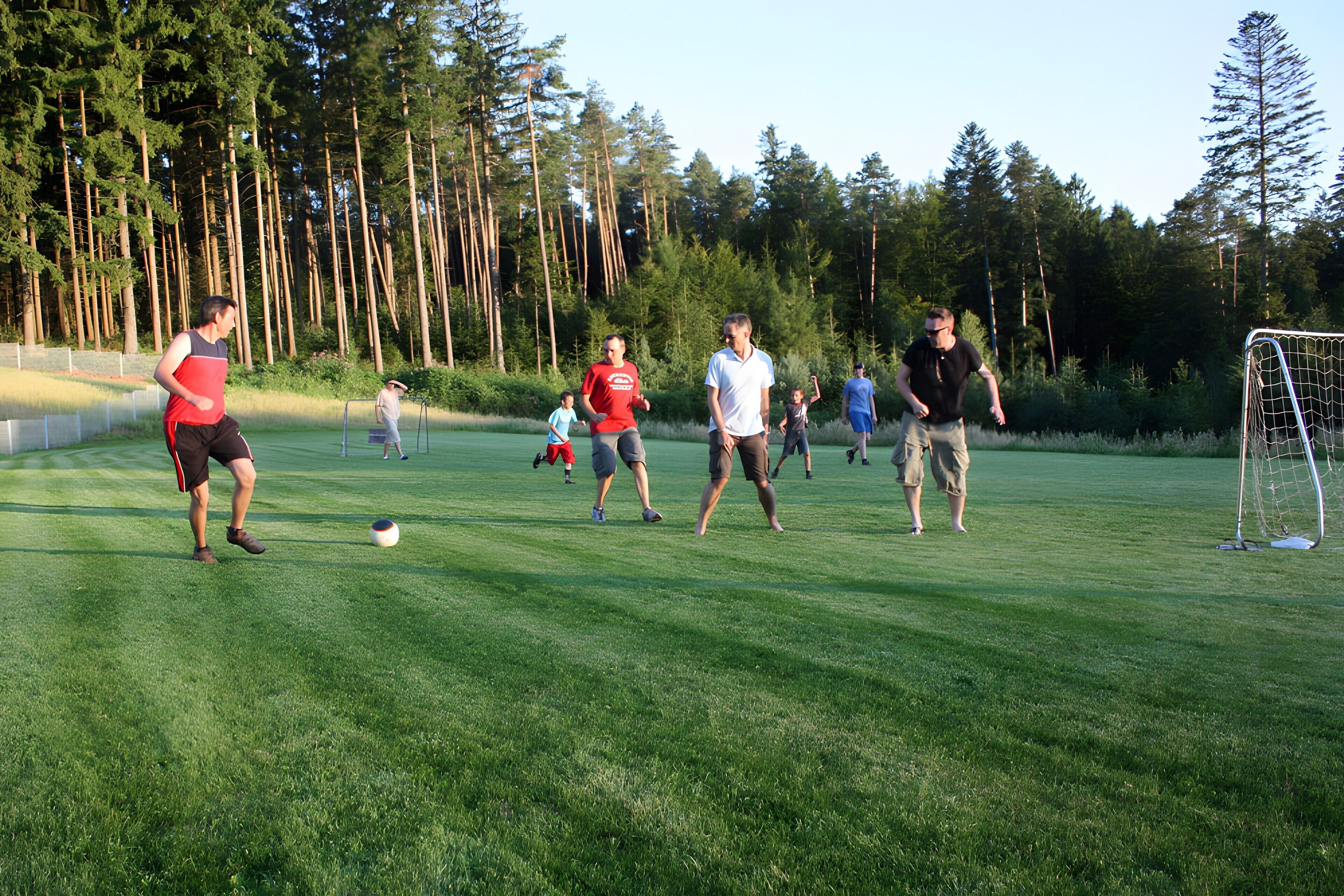 A group of people playing soccer on a grassy field with trees in the background.