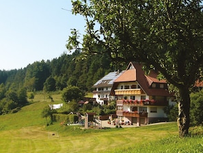 A two-story building with a sloped roof, solar panels, and a balcony with red railings. - Apartment 'Schlössle, 22 sqm' with Shared Terrace, Shared Garden and Wi-Fi (Elzach)