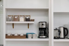 A kitchen with a coffee maker, a kettle, and jars of tea and coffee on shelves.