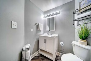 Une salle de bain avec un meuble-lavabo blanc, un miroir avec éclairage intégré, des toilettes et une plante.