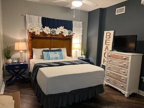 Une chambre à coucher comprenant un lit, des tables de chevet, une commode, un téléviseur et un ventilateur de plafond.