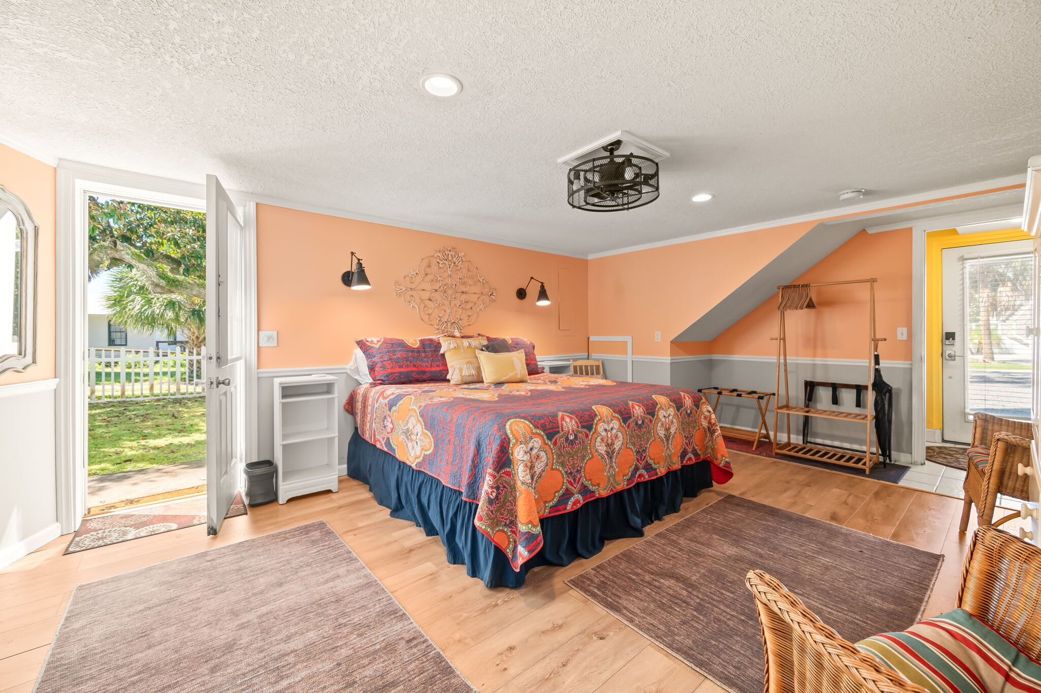 Ein Schlafzimmer mit einem großen Bett, Holzboden, Deckenventilator und Blick ins Freie.
