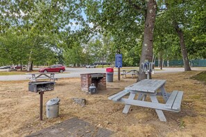Un área de picnic con un horno de ladrillo, mesas y un cubo de basura.