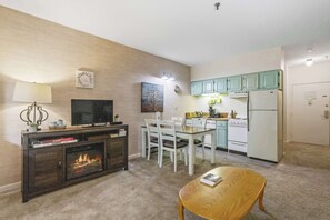 A living room with a fireplace, a television, a dining table with chairs, and a kitchen area with cabinets and appliances.