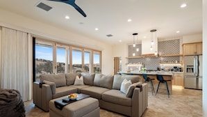 A modern living room with a sectional sofa, a coffee table with fruit, and a view of the kitchen in the background. - Vineyard Views + Covered Patio | Paso Robles | Mission de los Robles (Paso Robles)