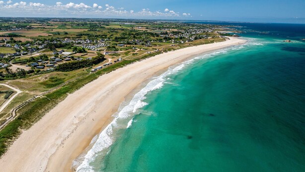 Une vue aérienne d’une zone côtière avec une plage, des maisons et de la végétation.