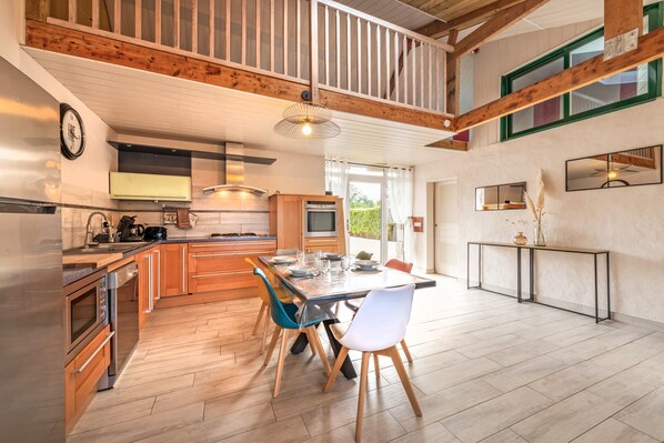 A modern kitchen with wooden beams, a dining area with chairs, and a large window.