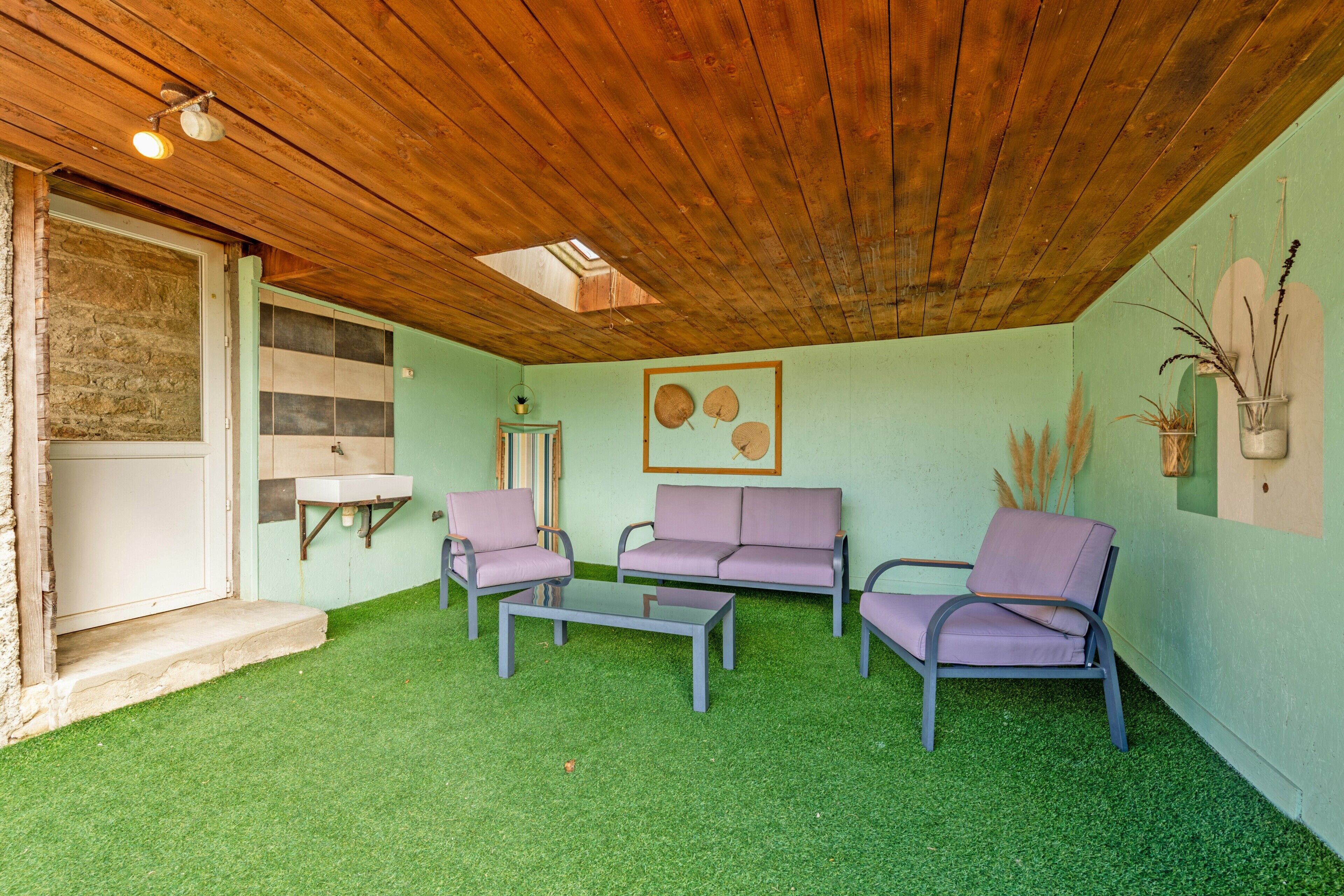 A room with a wooden ceiling, green artificial grass, a sofa, a coffee table, and a wall-mounted shelf.