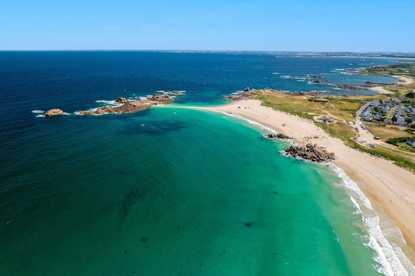 An aerial view of a coastal area with a beach, clear waters, and a residential area with houses.
