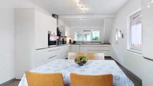 A modern kitchen with white cabinets, a dining table with chairs, and a window with a view of greenery. - Apartment 'Weinbergblick' with Balcony and Wi-Fi (Auggen)