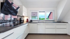 A modern kitchen with white cabinets, a black countertop, and a large window with a cityscape view. - Apartment 'Weinbergblick' with Balcony and Wi-Fi (Auggen)
