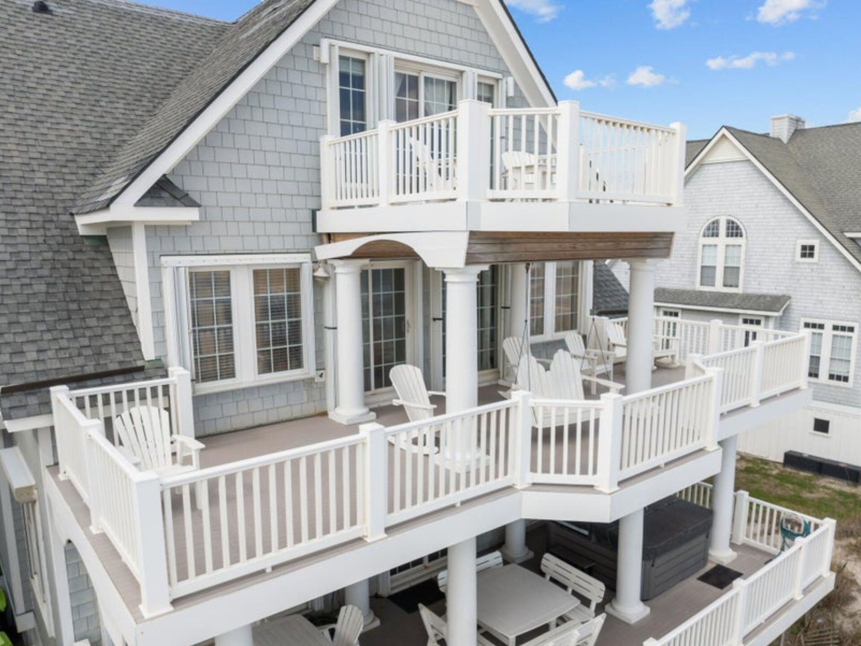 A two-story house with a covered porch, multiple windows, and outdoor seating.