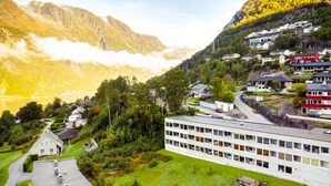 A modern building with a flat roof and multiple windows, surrounded by greenery and a mountainous backdrop. - Trolltunga Hostel (Ullensvang)