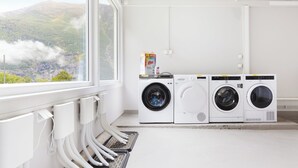 A laundry room with three stacked washers and dryers, a window with a view of mountains, and a white interior. - Trolltunga Hostel (Ullensvang)