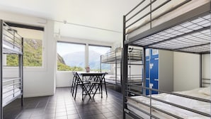 A dormitory room with bunk beds, a table, chairs, and a window with a mountain view. - Trolltunga Hostel (Ullensvang)
