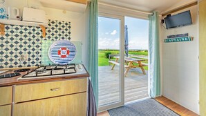 A kitchen with a gas stove, a kettle, and a wall-mounted TV. - Mobile Home 'Ty Reuniou' with Sea View, Private Terrace and Garden (Cléder)