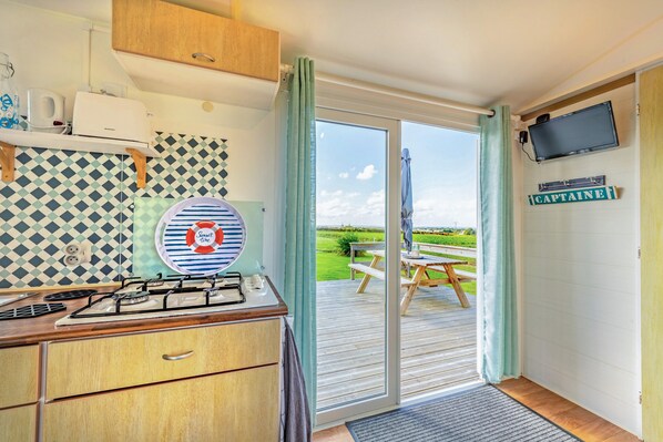 A kitchen with a gas stove, a kettle, and a wall-mounted TV.