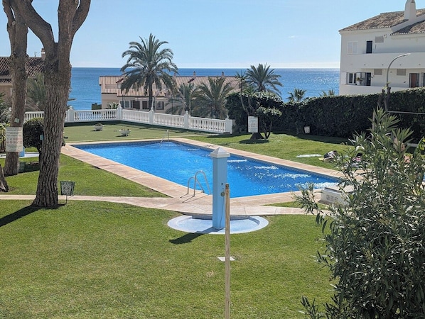 A swimming pool with a white fence, palm trees, and a view of the sea. - Lovely apartment by the beach with seaview & pool (Benalmadena)