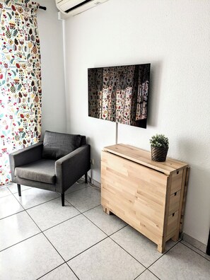 A modern room with a grey armchair, a wooden cabinet, and a wall-mounted TV. - Lovely apartment by the beach with seaview & pool (Benalmadena)