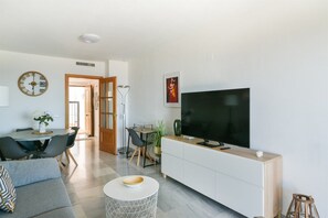 A modern living room with a flat-screen TV, a dining area with a table and chairs, and a sofa.