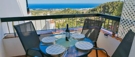 A balcony with a table set for four, overlooking a coastal landscape.