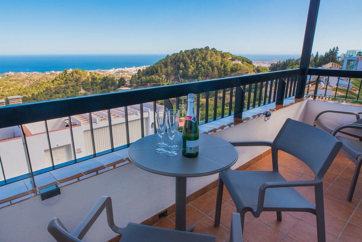 Een balkon met een tafel en stoelen, een fles champagne en uitzicht op zee en het landschap.