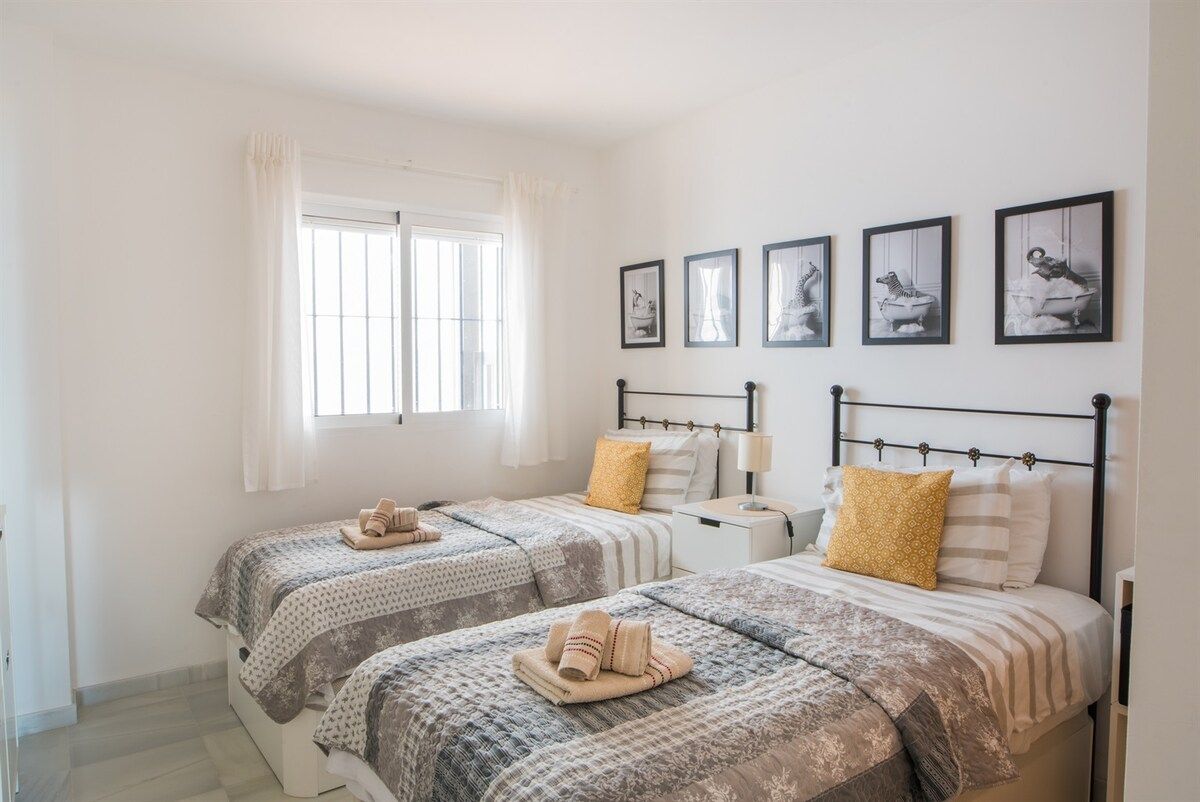 Un dormitorio con dos camas, una ventana con cortinas y una obra de arte colgada en la pared.
