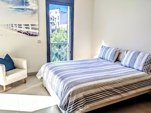 A bedroom with a bed, a chair, and a window with a view of buildings and trees.