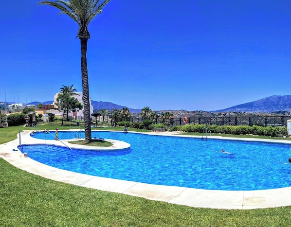 A swimming pool with a palm tree, surrounded by a fence, and a view of mountains in the background. - Sea view from 3 terraces / Beach 10min / Hot tub (La Cala de Mijas)