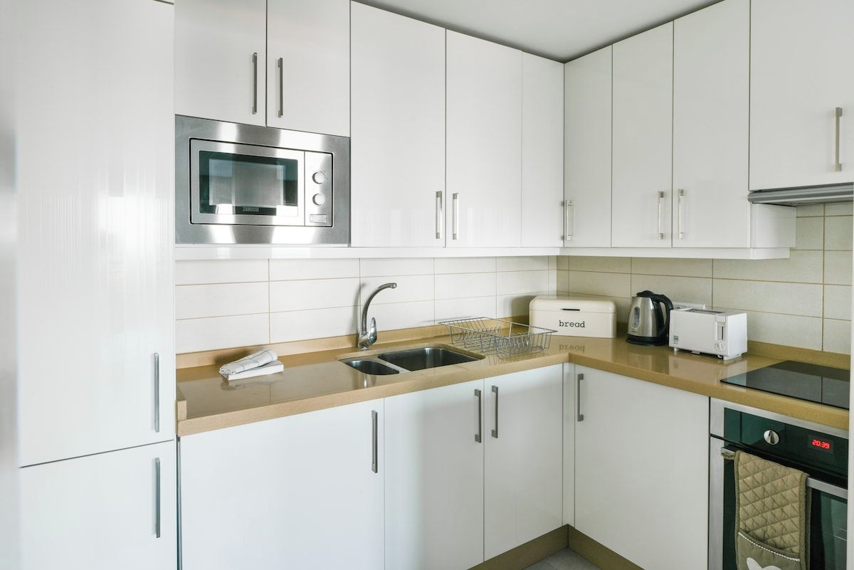 A modern kitchen with white cabinets, stainless steel appliances, and a built-in oven.