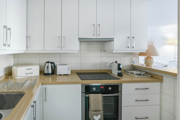 Una cocina moderna con armarios blancos, una encimera, un panero, un hervidor, un tostador, una estufa y un escurreplatos.