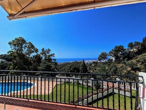 Piscina con vista al mar, rodeada de vegetación y una valla.