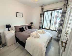 Un dormitorio con cama, mesitas de noche, un calentador y una ventana con cortinas.
