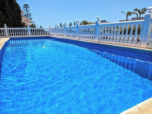 A clear blue swimming pool with a white fence and palm trees in the background.