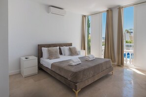 A bedroom with a bed, a bedside table, and a view of the outside.