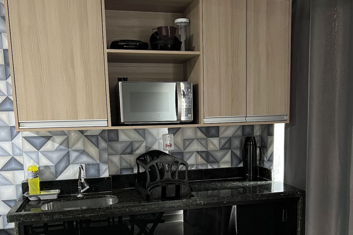 A compact kitchen with wooden cabinets, a microwave, a kettle, and a sink.