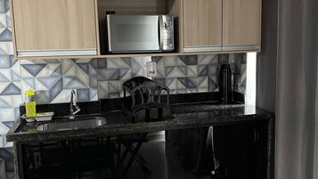 A compact kitchen with wooden cabinets, a microwave, a kettle, and a sink.