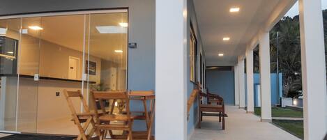Un pasillo moderno de hotel con puertas de cristal que dan a una habitación, sillas de madera afuera y vistas al exterior.