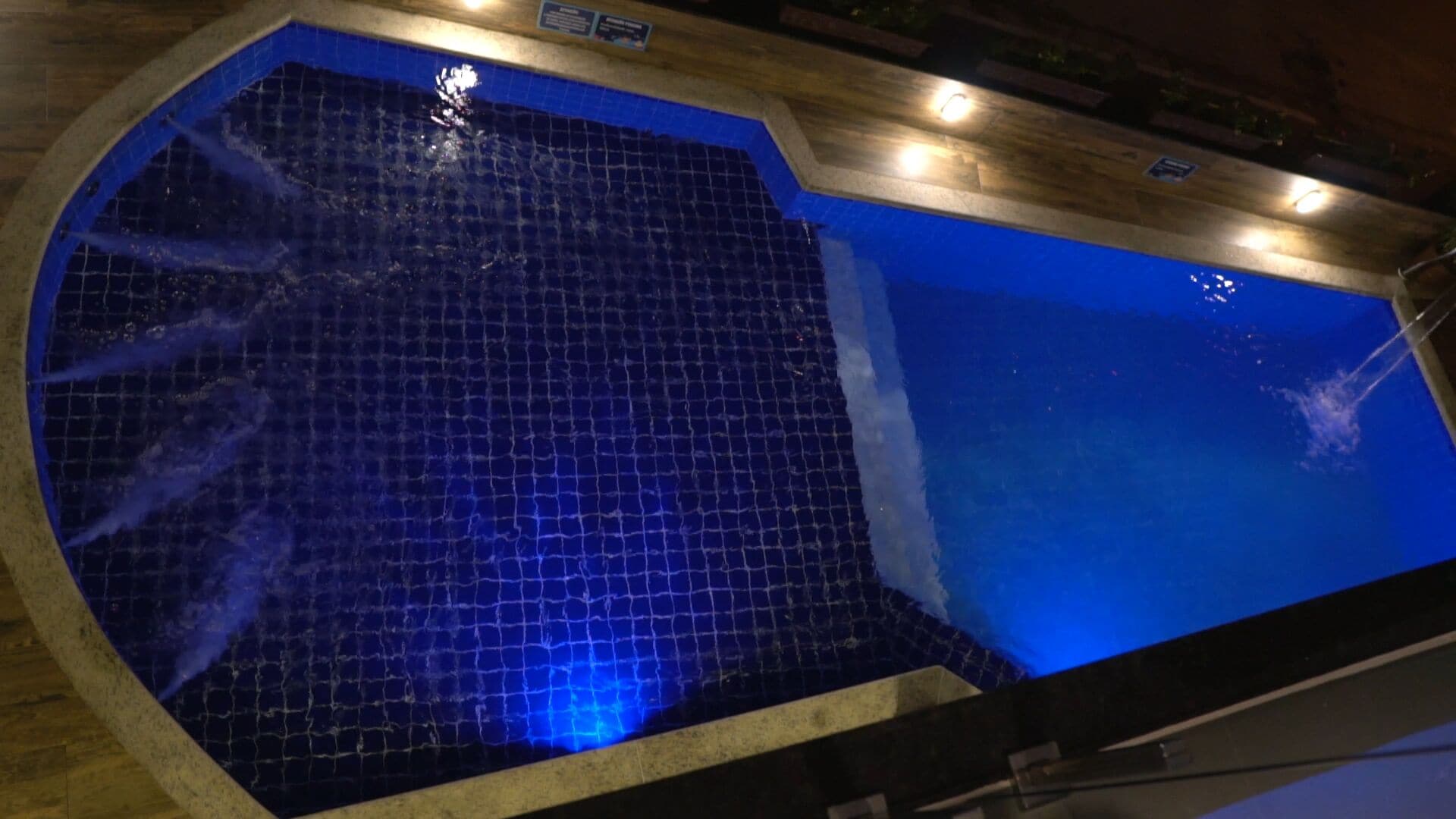 A swimming pool with a blue tiled floor and a wooden deck surrounding it.