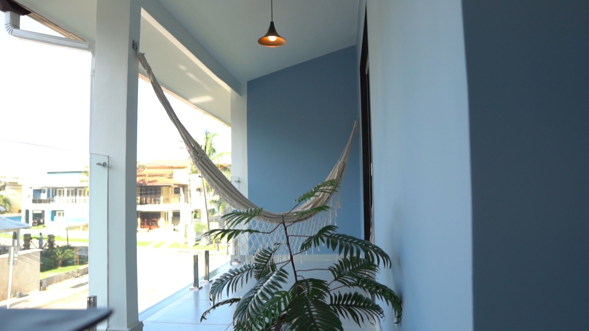 Une pièce avec un hamac, une plante en pot et une vue sur les bâtiments environnants.