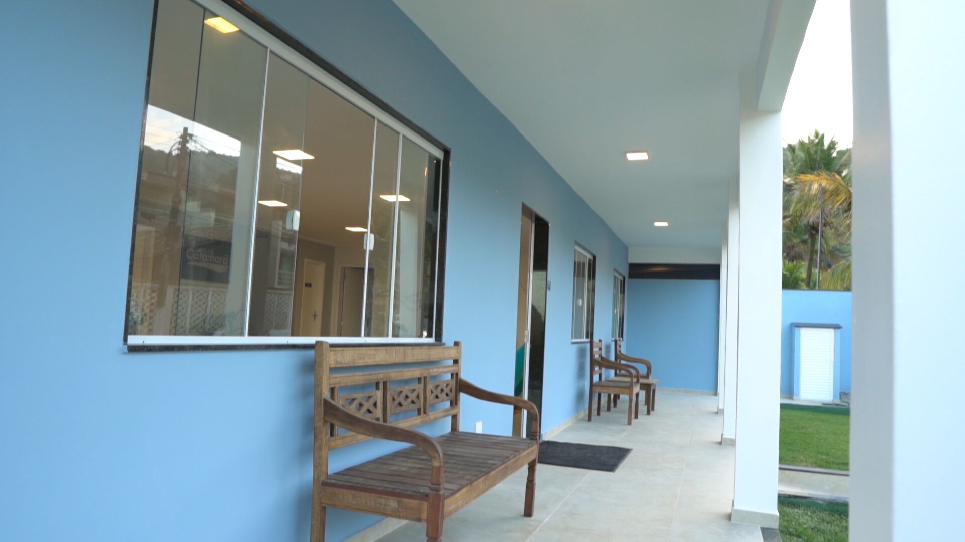 Um espaço ao ar livre coberto, com um banco de madeira, piso de azulejos e parede azul.