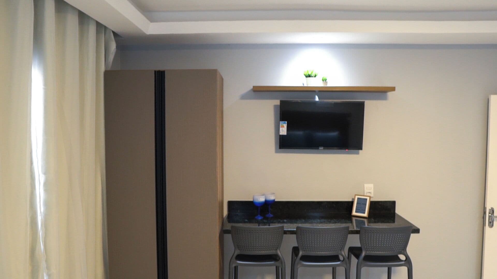 A compact kitchen with a refrigerator, a microwave, and a small bar area with two chairs and a counter.