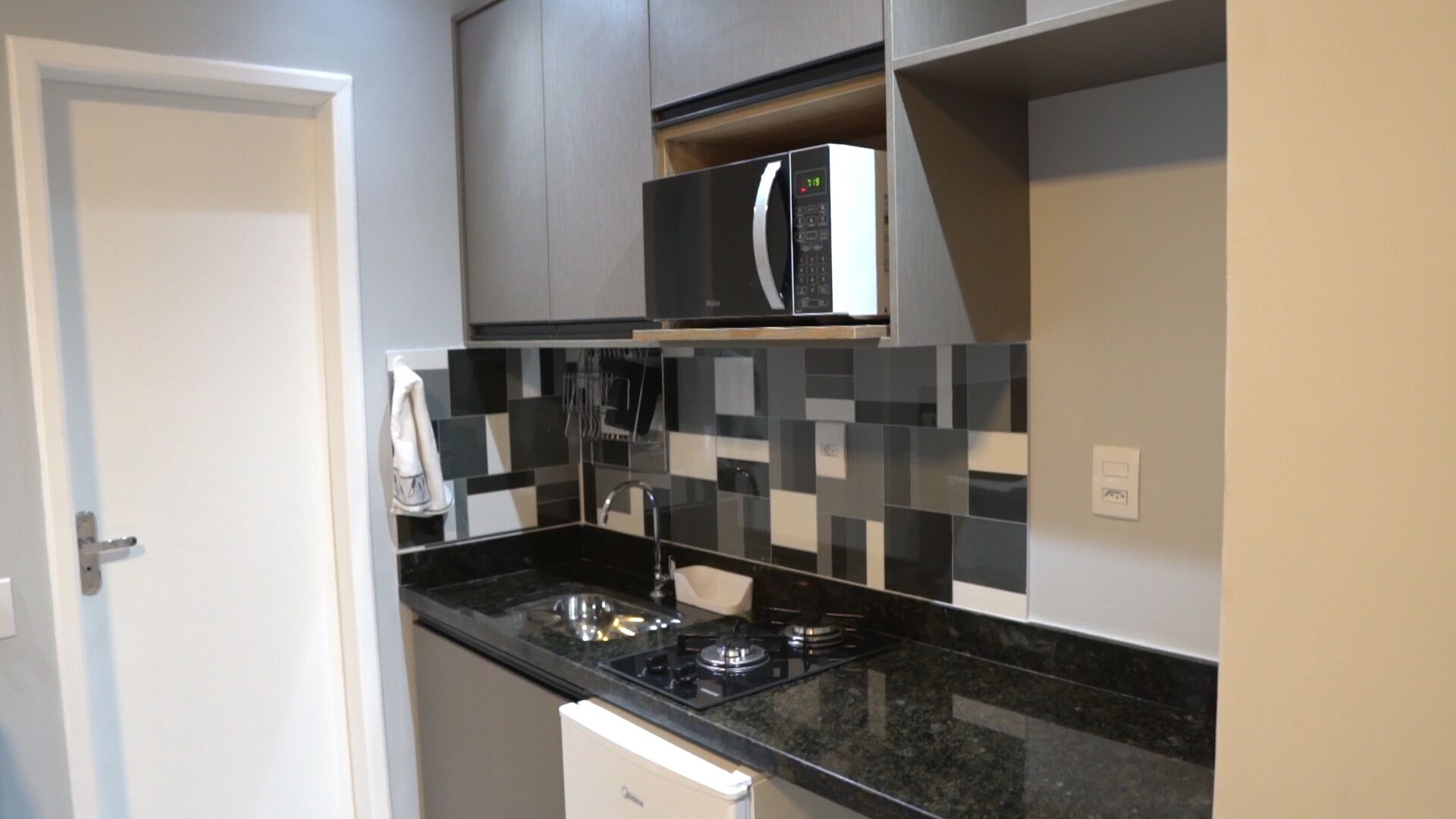 A compact kitchen with a black countertop, a gas stove, a microwave, and a tiled backsplash.