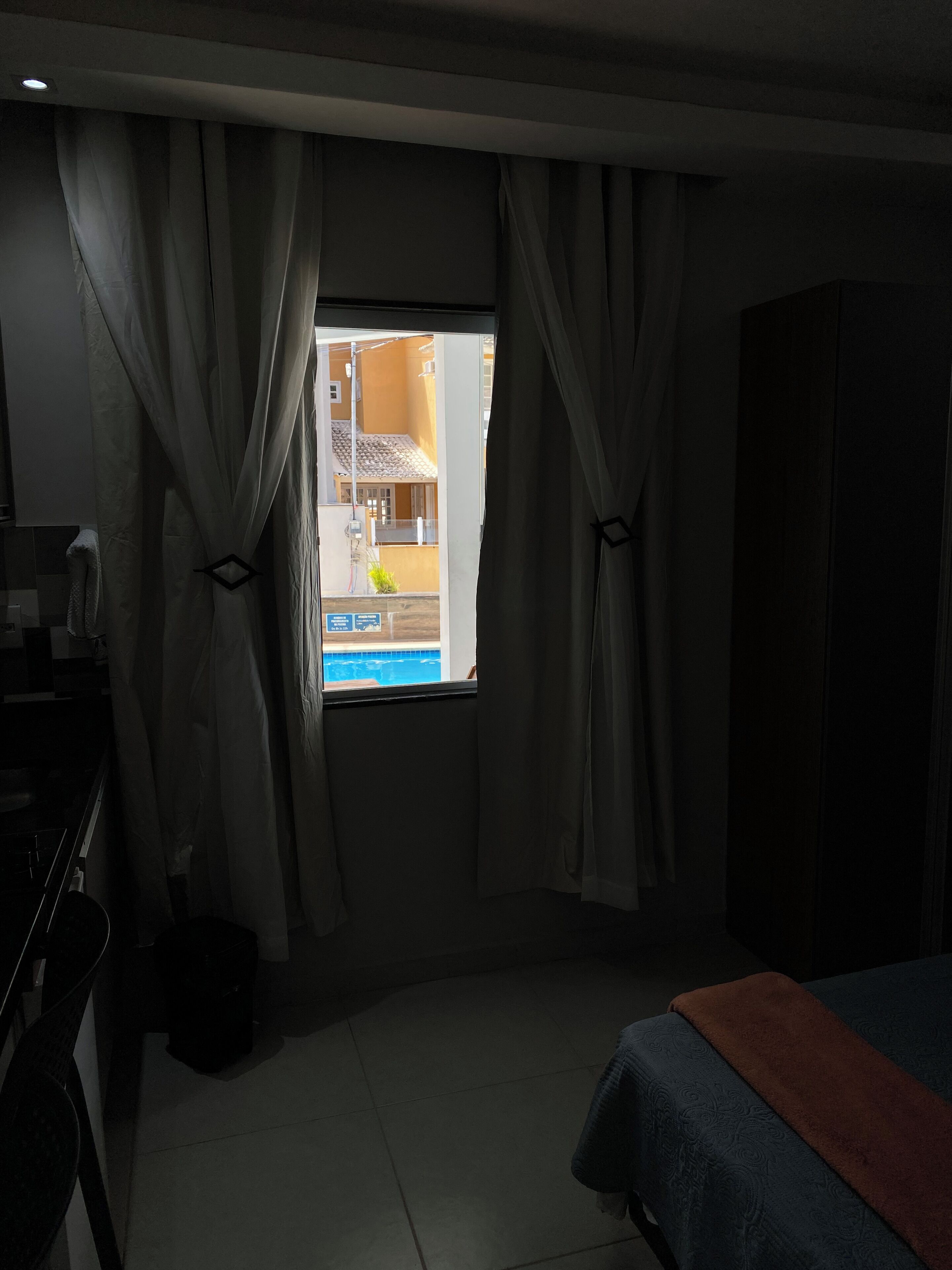 Habitació d'hotel amb un llit, una finestra amb cortines, vista a una piscina i una petita cuina.