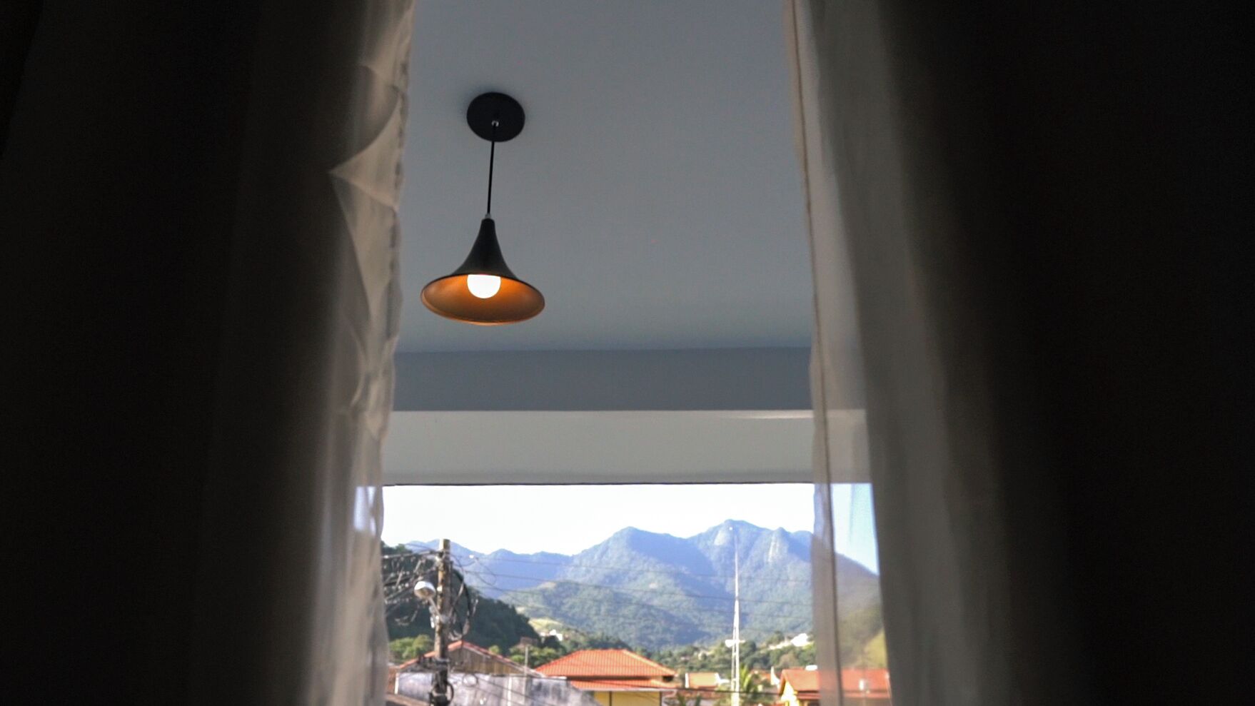 Een kamer met uitzicht op bergen door een raam, een hanglamp en gordijnen.