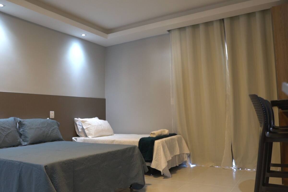 A hotel room with a bed, a small table, a chair, and a window with curtains.