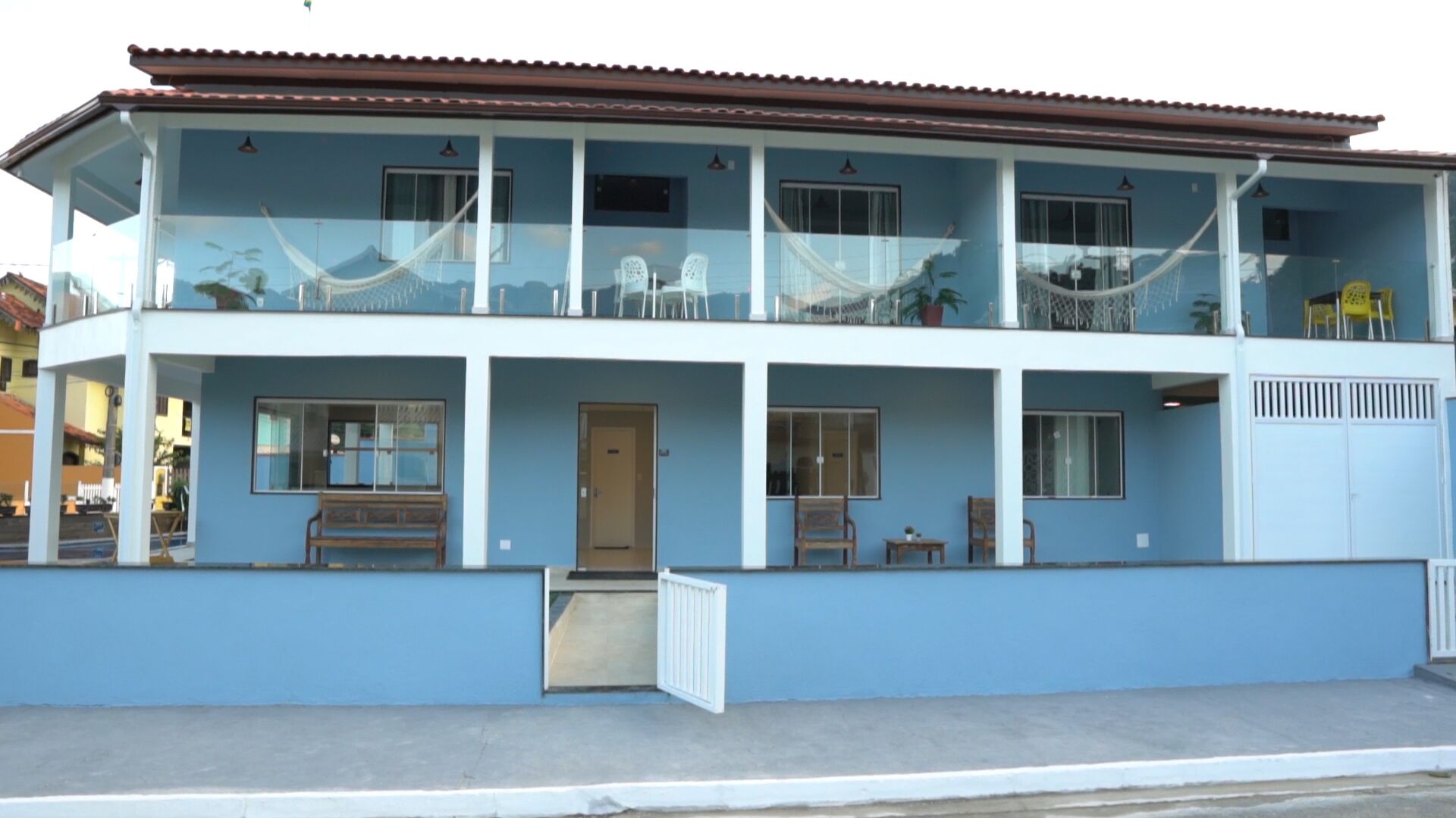 A two-story building with a balcony on the upper floor, a door on the ground floor, and a small porch area with a bench.