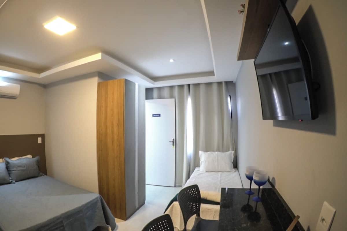 A hotel room with a bed, a desk, a chair, a TV, and a door.
