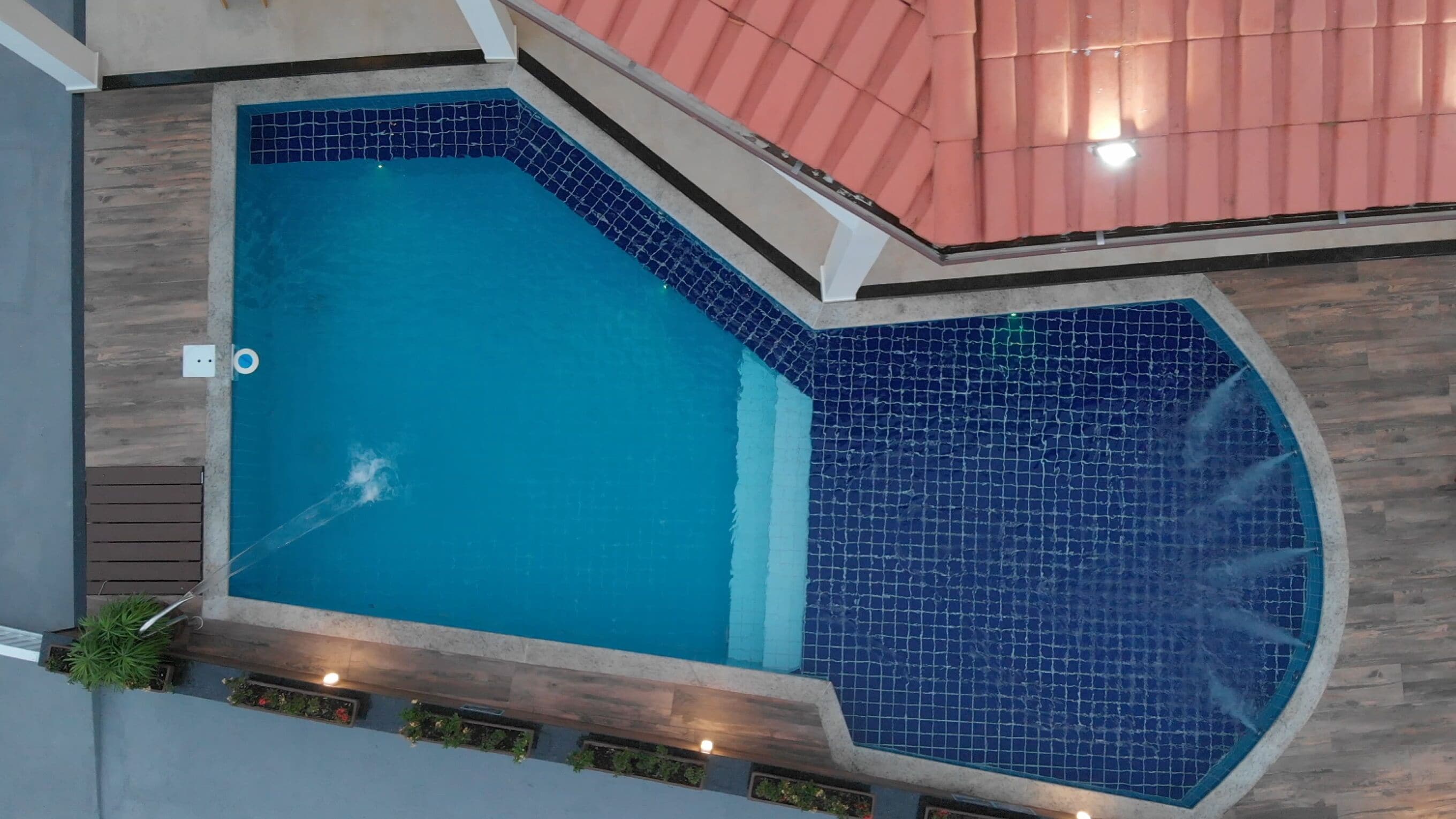 A large indoor swimming pool with a blue tiled interior, surrounded by wooden decking and a red roof.