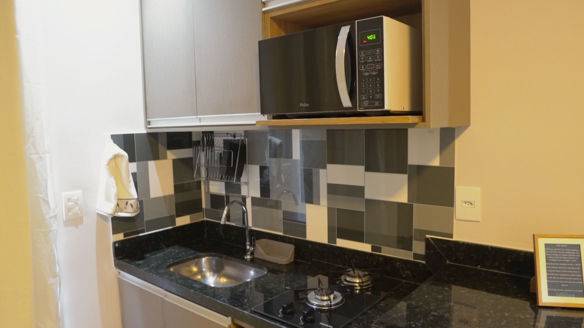 A compact kitchen with a black countertop, a stainless steel sink, a gas stove, a microwave, and a tiled backsplash.